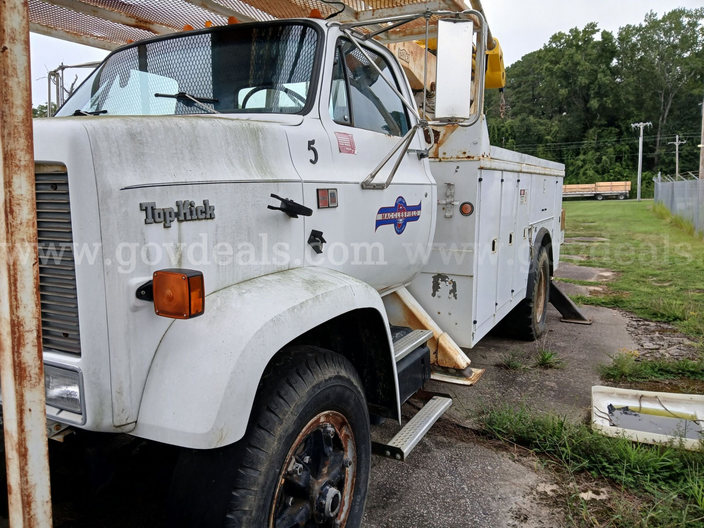 GMC 7000 bucket truck front left side with hydraulic crane, in-service.
Visible text: 'TopKick' on hood, orange turn signal, dual mirrors, badge with star logo on door, number 5.
