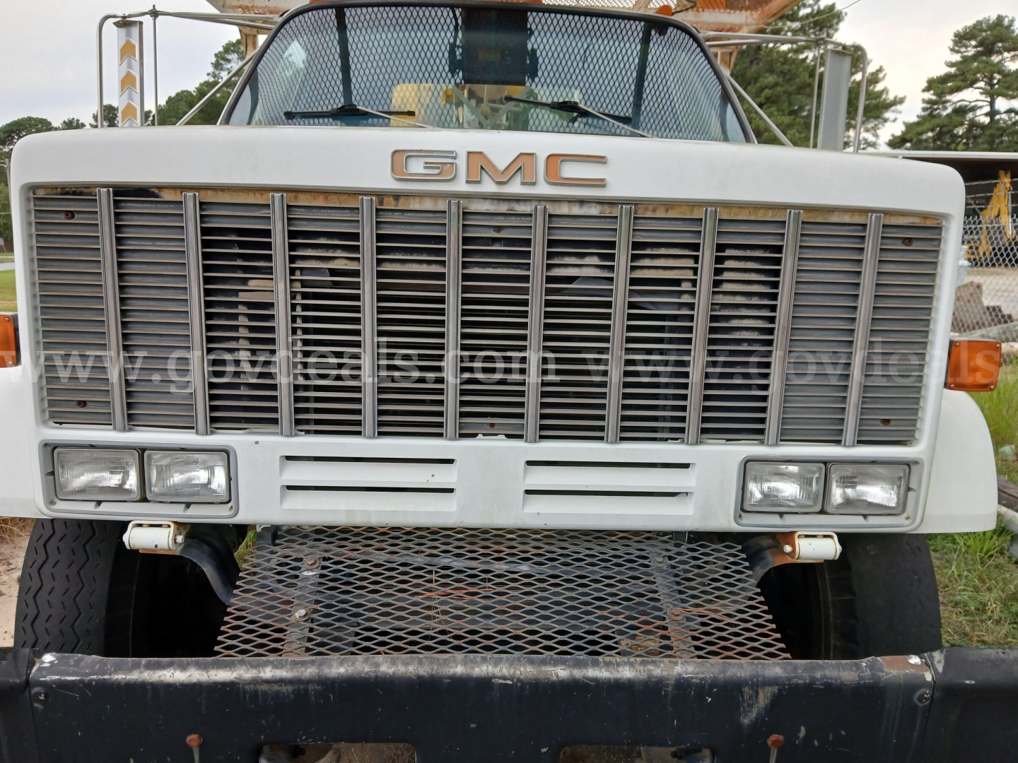 GMC truck front grille with large vertical slats and GMC emblem, rectangular headlights, metal bumper, and mesh guard visible.
