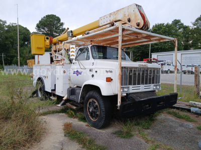 GMC bucket truck from 1986 with boom lift, white cab, black front bumper, showing service area and weathered signage.
