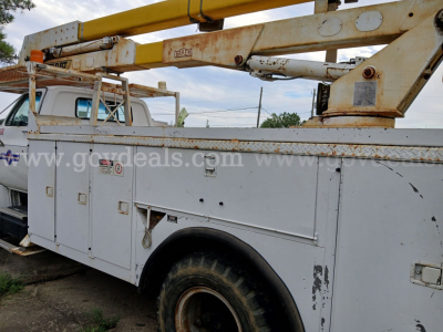GMC bucket truck with elevated work platform on utility body showing service compartments and worn paint.