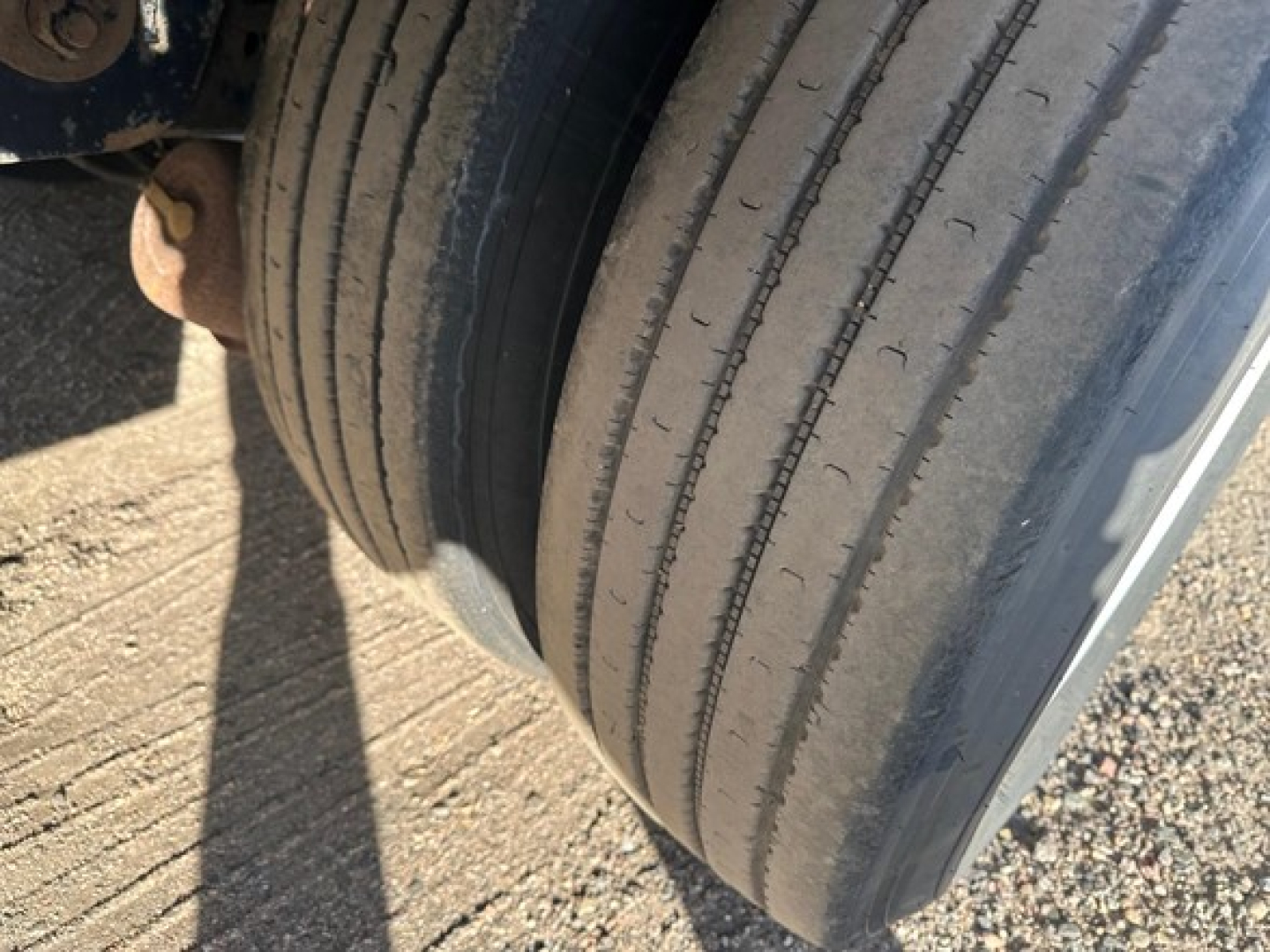 Trailer wheel and tire close-up showing multiple thin grooves; part of aluminum drop deck trailer components visible.