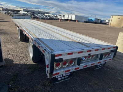Flatbed trailer from rear-right angle showing aluminum drop deck with taillights and bumper, Denver Colorado contact plate, UE11193 stock tag, 2018 Reitnouer Maxmiser label.