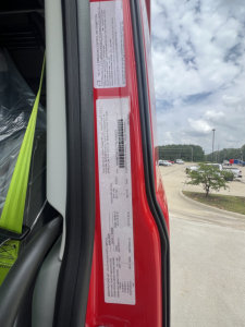 Stickering and VIN label area on the door jamb of a new Volvo VNL64T660 truck showing tall white labels with barcodes and text. Side door seal and window frame visible.
