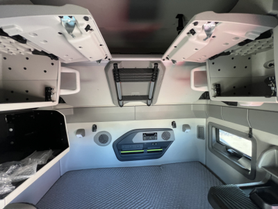 Interior cab of 2026 Volvo VNL64T660 sleeper with overhead storage shelves and bunk access, view from bed area showing windows, control panel, and storage compartments.