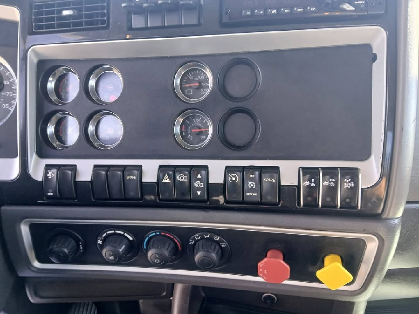 Dashboard panel of a 2018 Kenworth T800 showing gauges and switches with black panel and red/yellow warning knobs.