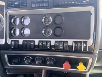 Dashboard panel of a 2018 Kenworth T800 showing gauges and switches with black panel and red/yellow warning knobs.
