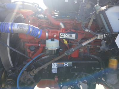 Kenworth T800 engine bay showing X15 Cummins badge and red engine with blue coolant hose and white reservoir.