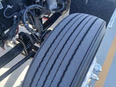 Kenworth T800 truck front wheel and suspension components visible in engine bay area; tire tread and wheel hub seen; various hoses and wiring in view.
