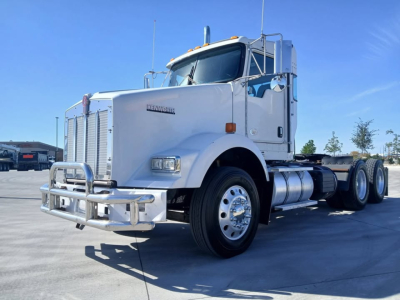 Kenworth T800 conventional sleeper truck in white front-side view showing chrome bumper grille and dual rear axles.