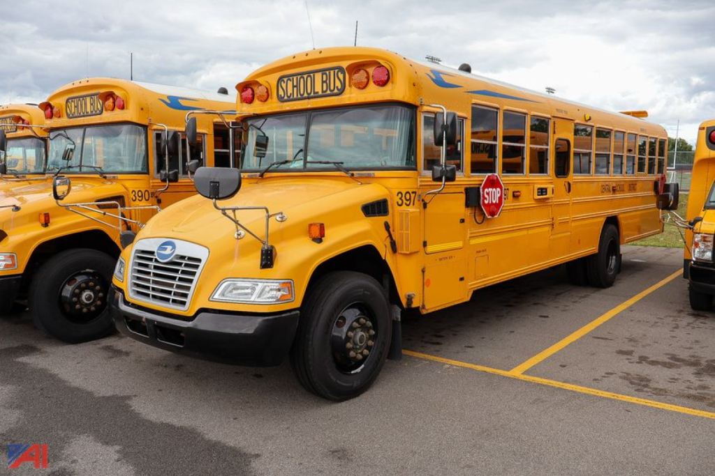 Two yellow 2018 Blue Bird Vision school buses parked side by side in a lot, front bus showing grill and stop sign, blue bird logo on hood.