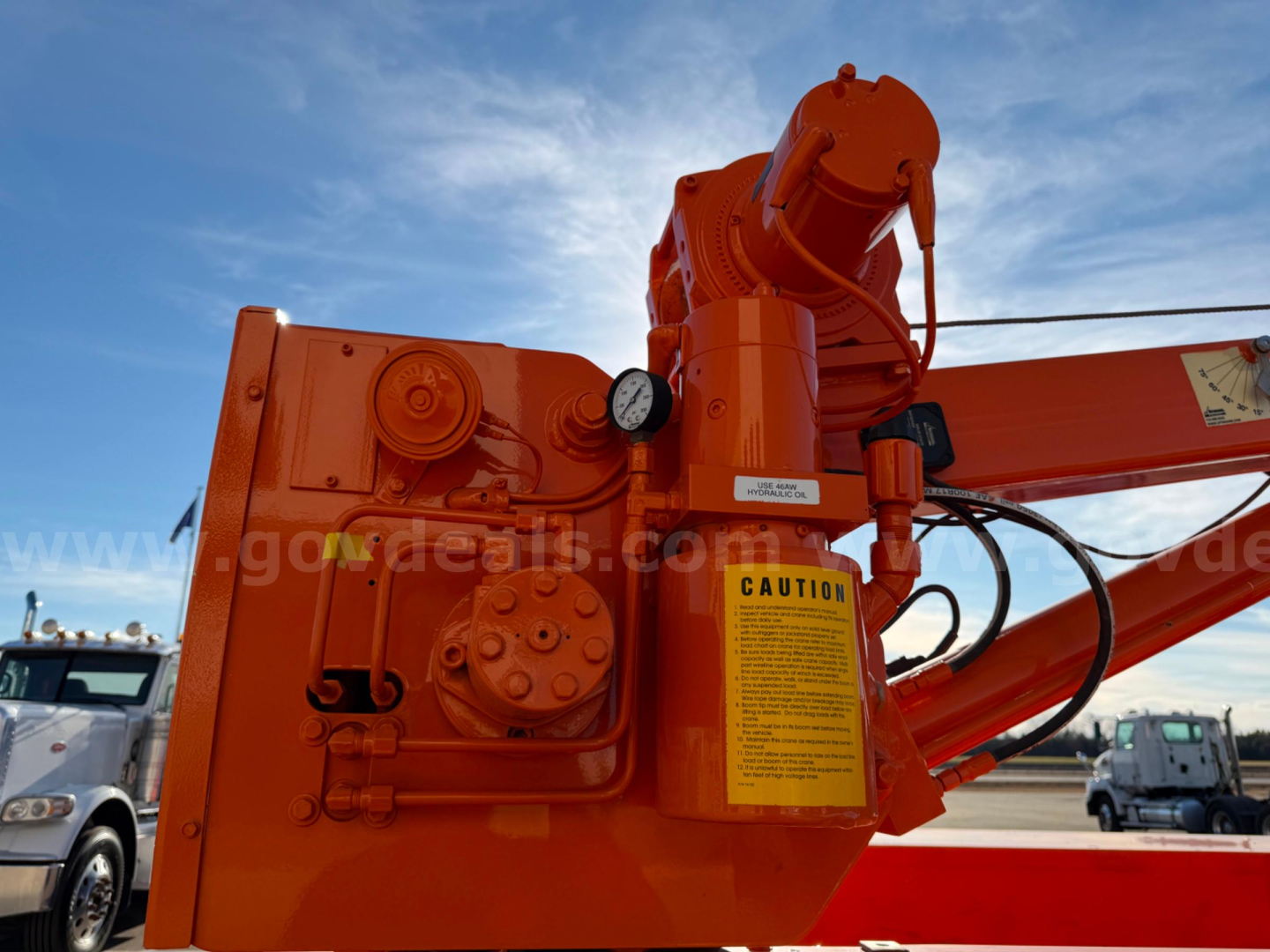Orange hydraulic crane arm with caution label and control housing visible, part of a Ram 3500 utility vehicle in a dealership lot.