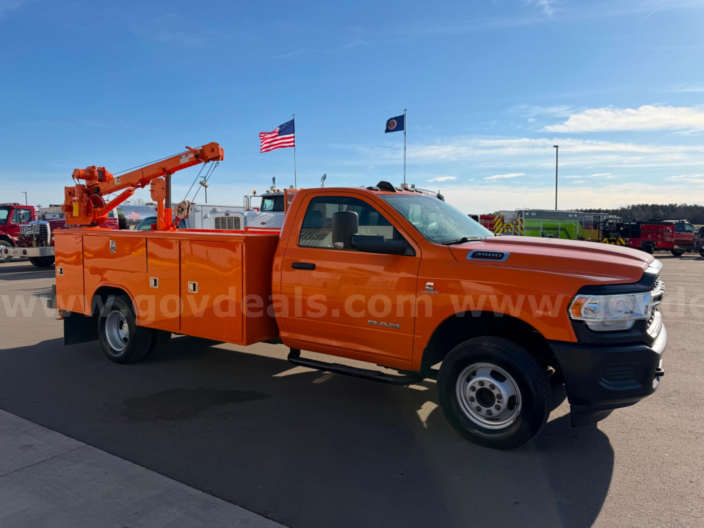 Orange Ram 3500 utility/service truck in a dealership lot, side view showing crane/boom on utility bed.