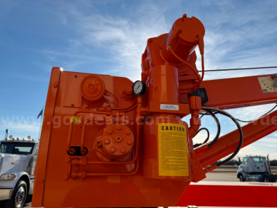 Orange hydraulic crane arm with caution label and control housing visible, part of a Ram 3500 utility vehicle in a dealership lot.