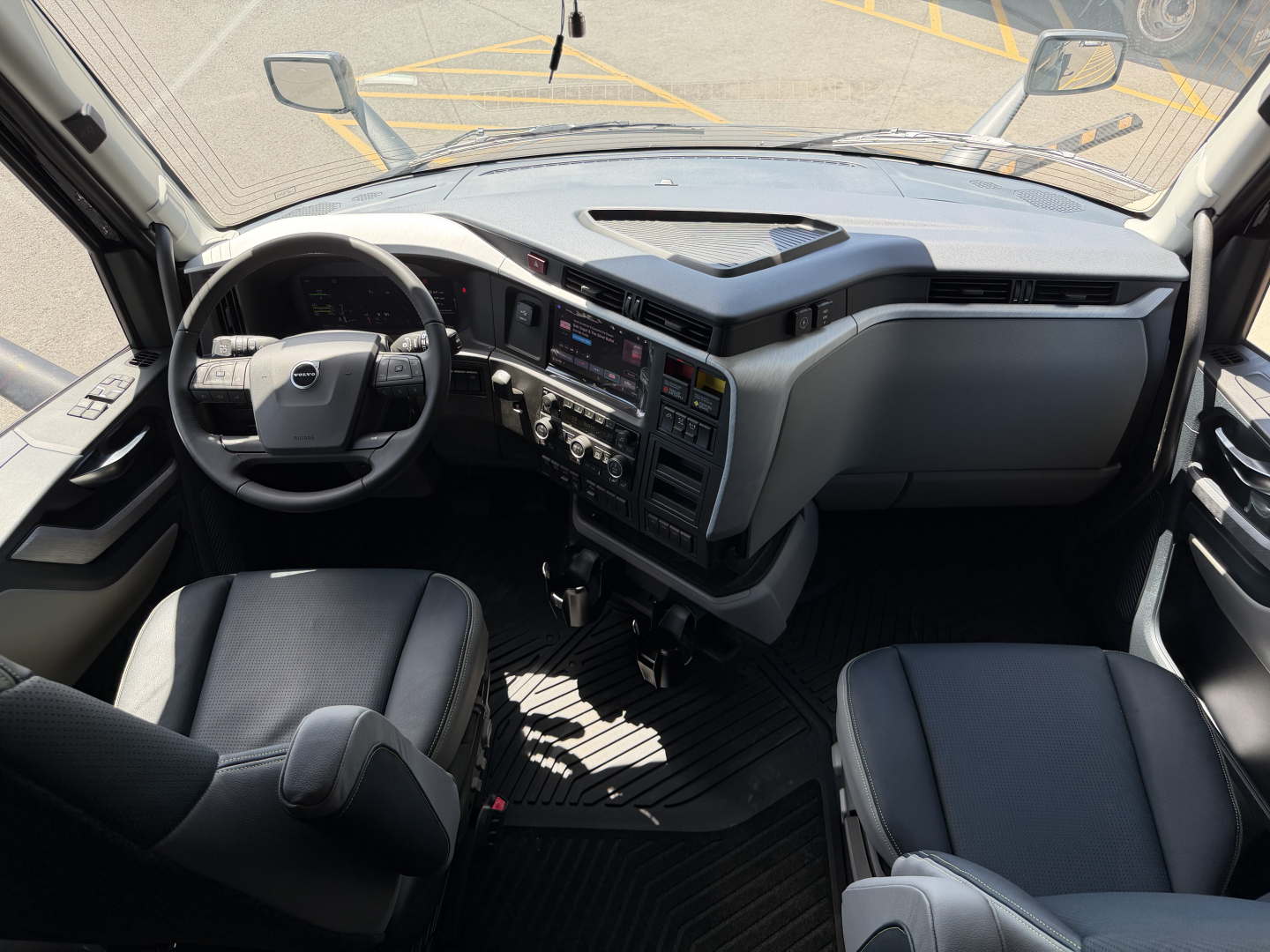 Truck cab interior of a Volvo VNL showing steering wheel, dashboard, and two front seats.