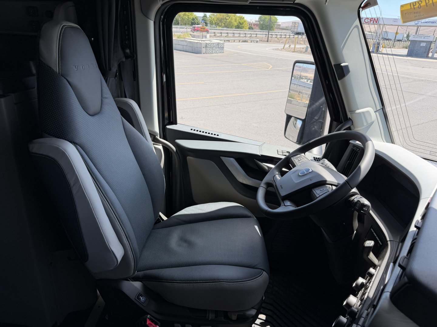 Cab interior of a Volvo VNL tractor showing driver seat and steering wheel, dashboard, and window view.