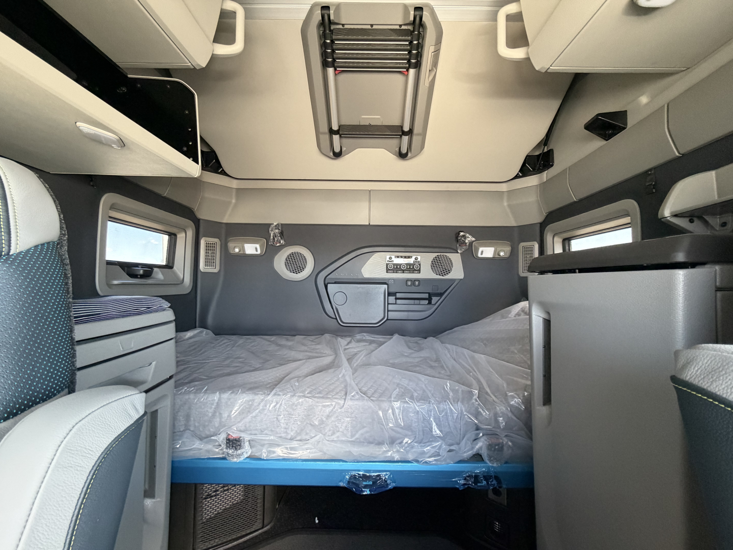 Volvo VNL64T860 sleeper cab interior with bed, storage cabinets, and overhead ladder in view.