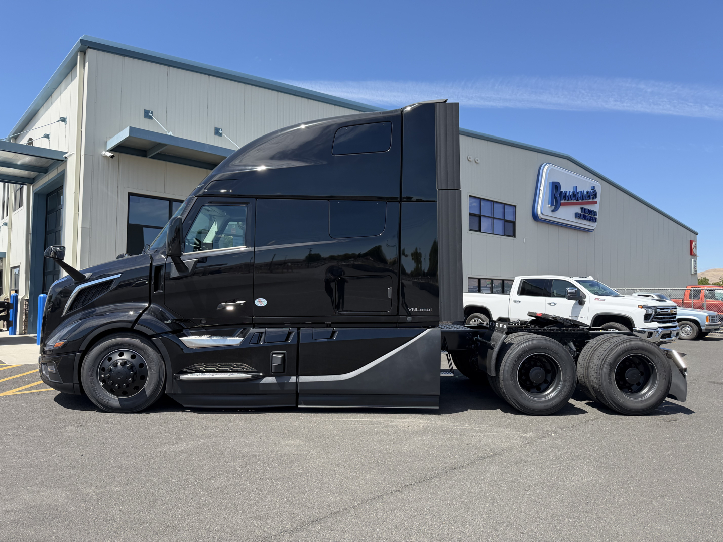 2027 Volvo VNL64T860 tractor-trailer in black with sleeper cab, three-axle configuration, parked in front of dealership building.