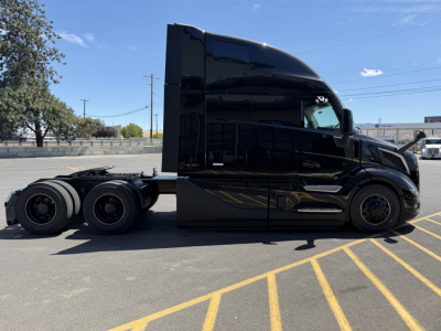 Volvo VNL64T860 cab facing left in a parking lot, glossy black paint, side view with sleeper cabin and rear wheels visible.