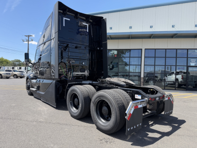 Volvo VNL64T860 cab with sleeper in black, rear view showing dual rear axles and fifth wheel, external of dealership.