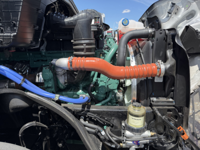 Volvo engine bay with orange flexible hose, blue line, green engine block, and Volvo hydraulic reservoir visible.