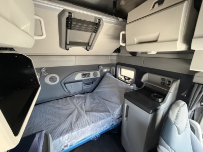 Volvo VNL sleeper cab interior showing bunk bed with plastic cover, overhead storage, cabinets, and control panel near window.