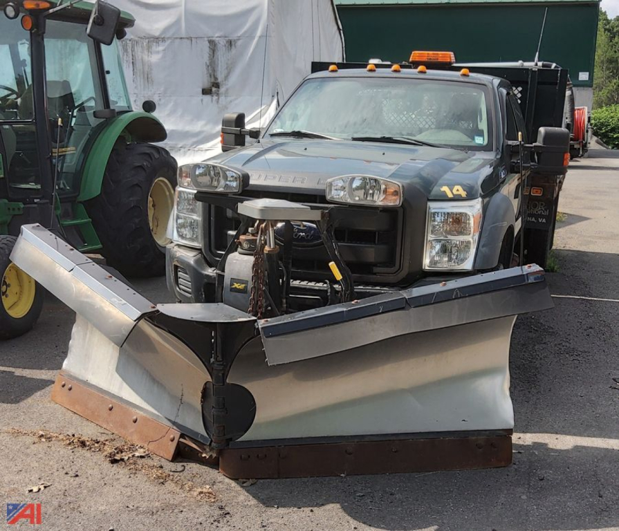 Ford F-450 Super Duty extended cab flatbed with front mounted snow plow, in-service vehicle, showing plow blade and mounting hardware.