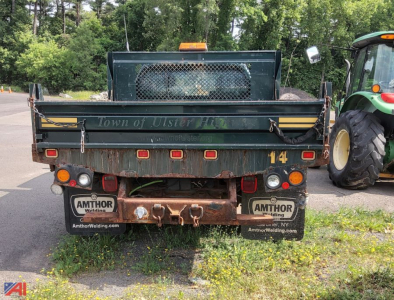 Rear view of a green Ford F-450 flatbed truck with a plow, showing taillights, bumper, and Amthor Welding license plate frames.