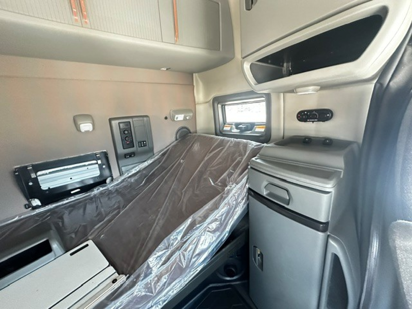 Interior of a Volvo VNL64T740 sleeper cab showing deployed bed, side storage, window view, and dashboard panels.