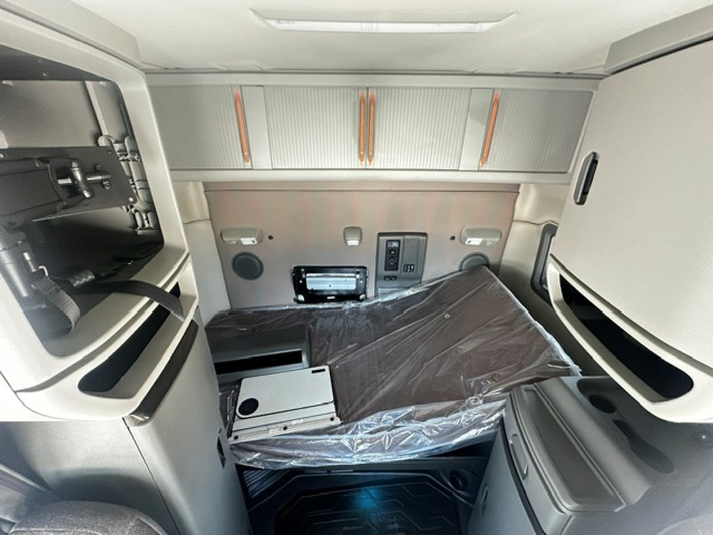 Volvo VNL64T740 sleeper cab interior showing dashboard area, storage cabinets, and passenger seat covered in plastic.