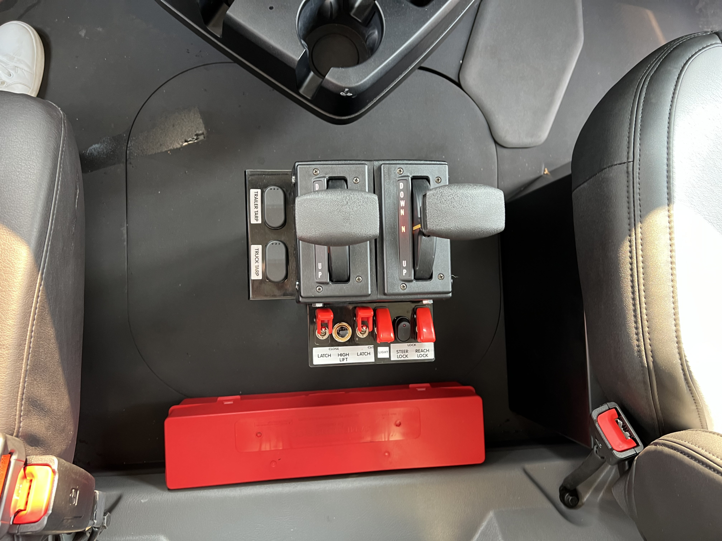 Mack GR84F truck interior center console with two joystick controls and red storage bin beneath. Visible labels on levers and panels.
