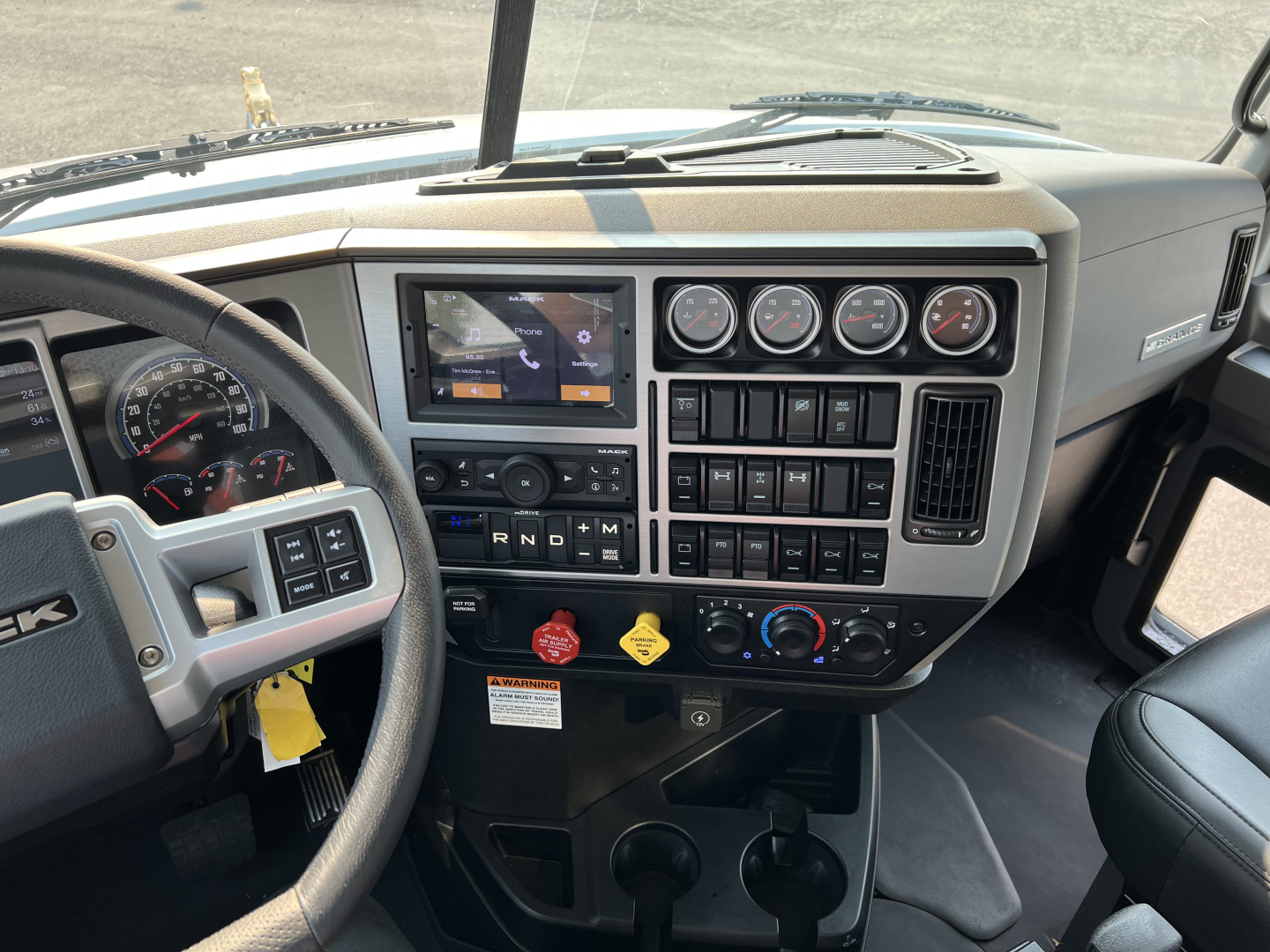 Dashboard interior of a 2027 Mack GR84F dump truck showing steering wheel, multiple gauges, infotainment screen, climate controls, and gear selector panel.