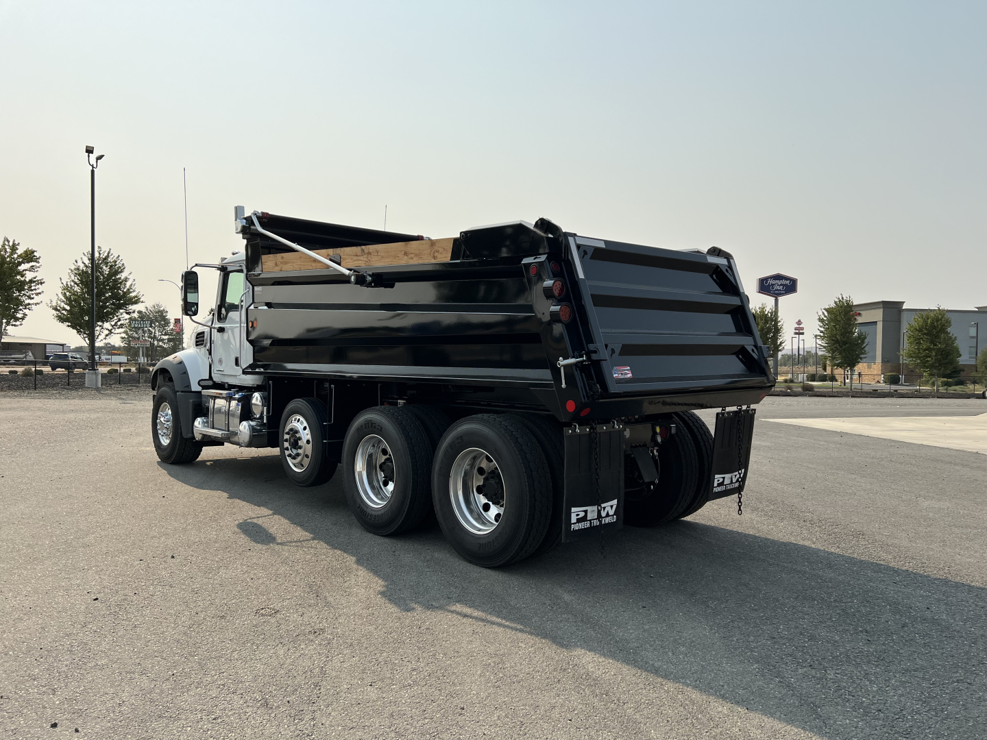 Dump truck rear view showing oversized dump bed and triple rear axles with mud flaps and hydraulic lift mechanism.