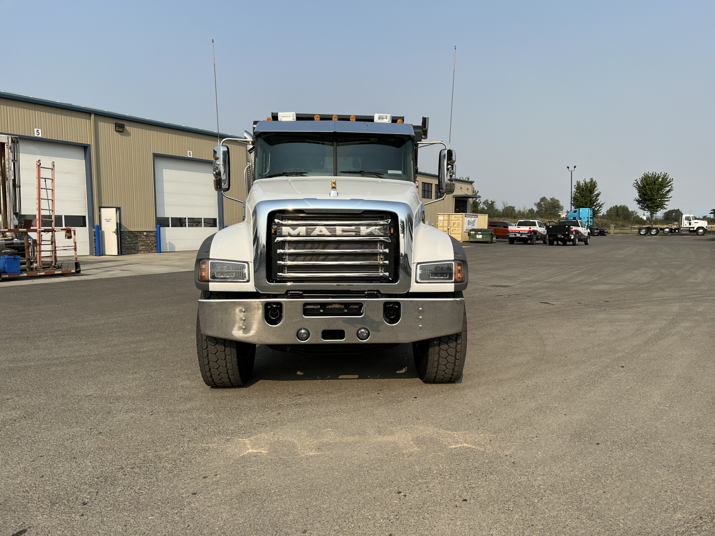Front view of a white Mack truck with large grille showing the word MACK on grille. Front bumper with black tow hooks, headlights, and brand badge visible.