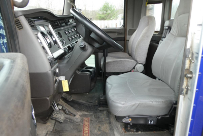 Truck cab interior of a 2013 Kenworth T660 conventional daycab showing steering wheel, dashboard, driver seat, and passenger seat.