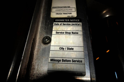 Identification label on truck door area showing fields: IDENTIFICATION NO., TRUCK TRACTOR, ODOMETER NOTICE, Date of Service (m/d/yr), Service Shop Name, City / State, Mileage Before Service.