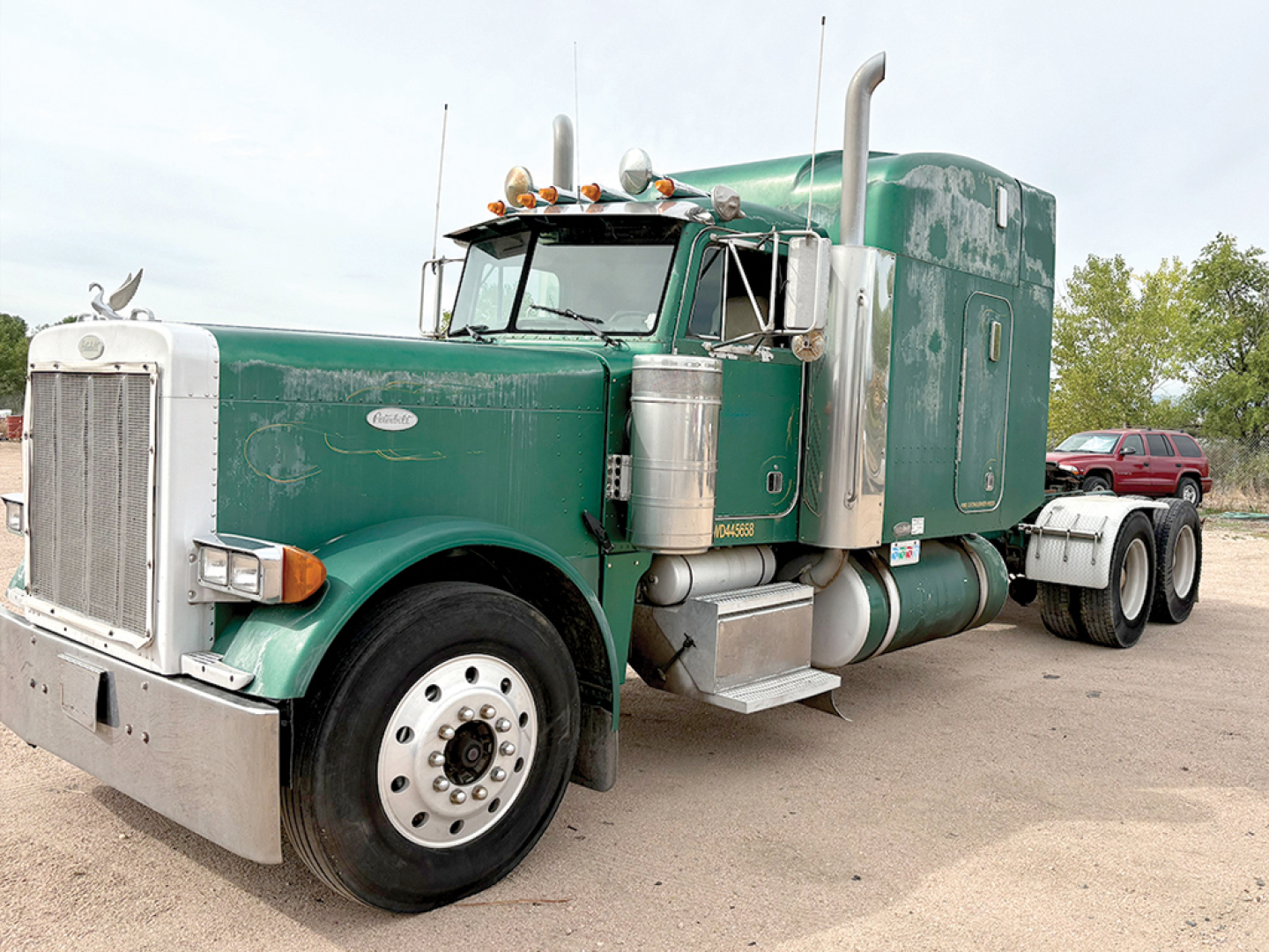 Peterbilt 379 tractor-trailer with extended hood in green and white, front grille, chrome fuel tanks, and sleeper cab.