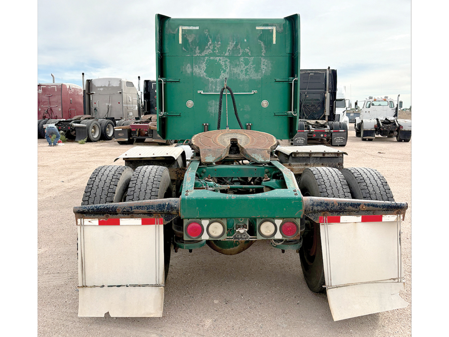 Truck rear view showing fifth wheel, dual rear axles, green frame, and white mud flaps on a Peterbilt 379 cab-over engine bay.