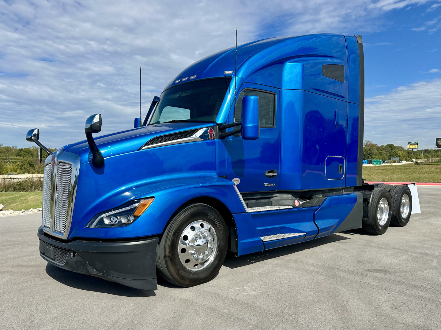 Kenworth T680 tractor in blue profile view showing large sleeper cab and chrome fuel tanks.