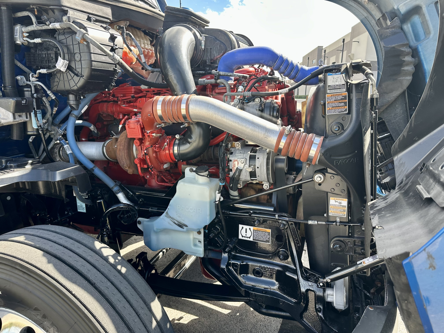 Kenworth T680 engine bay with red engine block, large silver intake piping, blue hoses, and black chassis components visible.