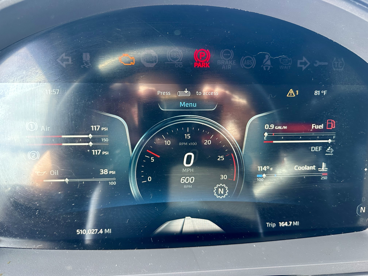 Instrument cluster of a 2023 Kenworth T680 showing digital gauges and warning icons, center tachometer with 0 mph, left fuel and oil gauges, right DEF and coolant indicators, Trip 164.7 Mi.
