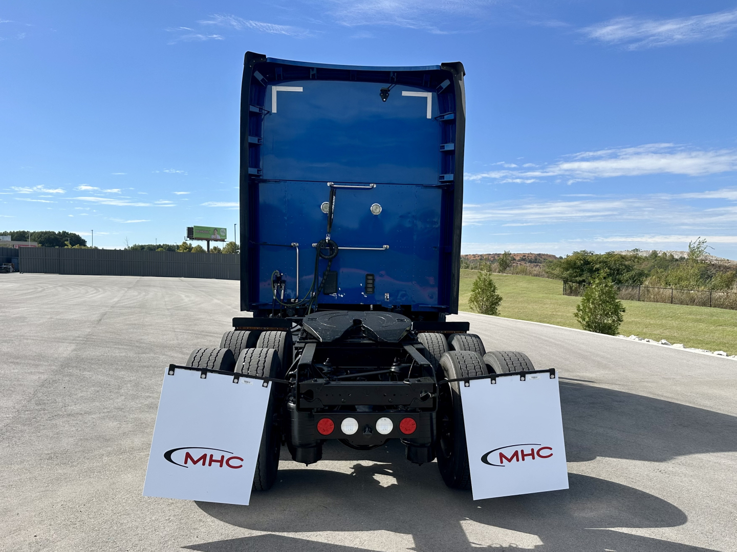 Kenworth T680 rear view showing blue sleeper cab and white MHC mud flaps with red logos.