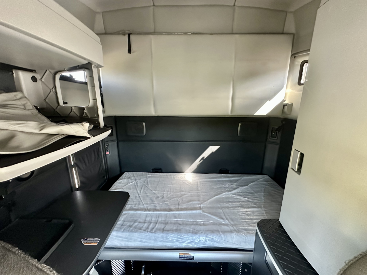Kenworth T680 sleeper cab interior showing bed platform with mattress, overhead storage, and side cabinet panels.