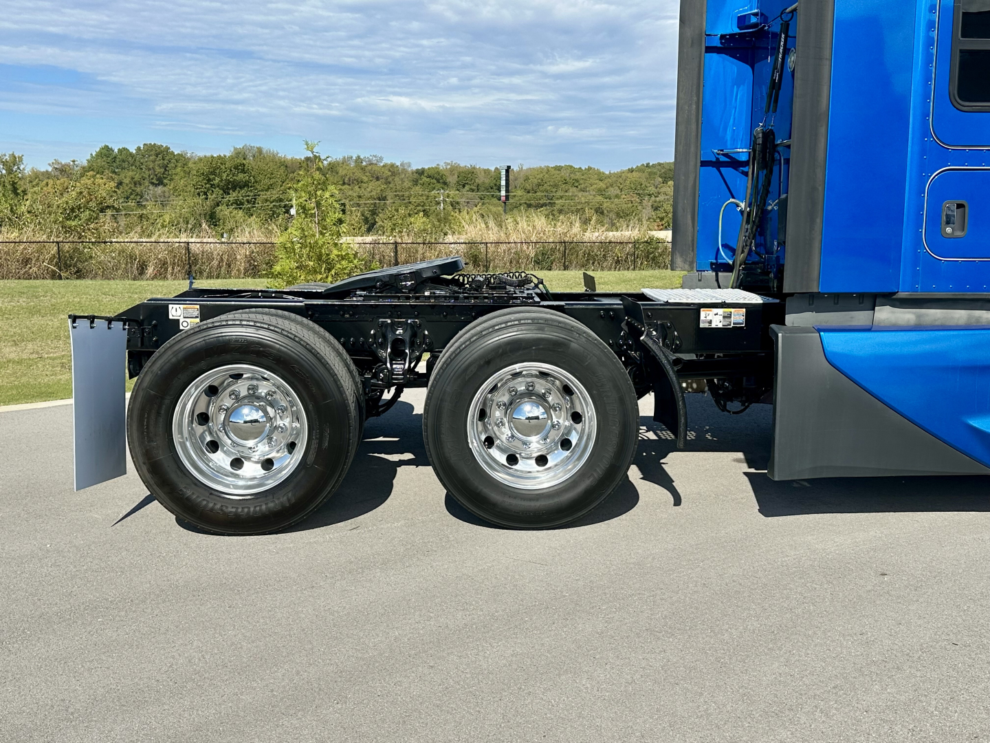 Twin rear axle of a blue Kenworth T680 tractor showing chrome wheels and chassis, side view.