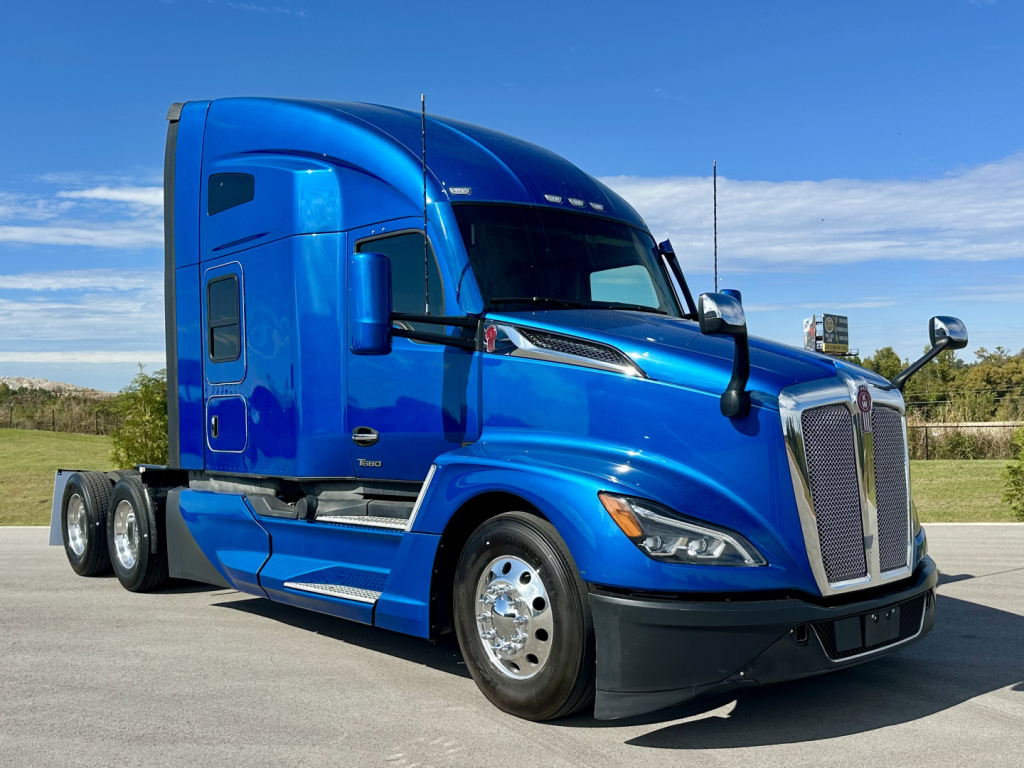 Kenworth T680 blue semi-truck in a parking lot, side view with cab, sleeper compartment, and chrome wheels.