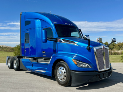 Kenworth T680 blue semi-truck in a parking lot, side view with cab, sleeper compartment, and chrome wheels.