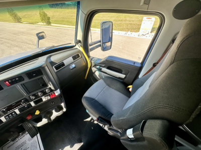 Kenworth T680 truck interior showing driver seat, steering wheel, dashboard, and center console viewed from passenger side in daytime.