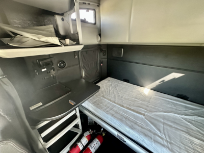 Kenworth T680 sleeper cab interior showing bunk bed with mattress, overhead storage, and control panels on left side.