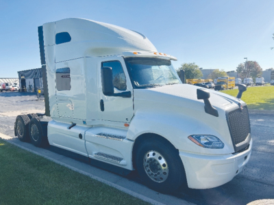 Truck cab view showing International LT625 with sleeper configuration, white exterior, large curved windshield, side mirrors, front grille, and dual rear wheels.