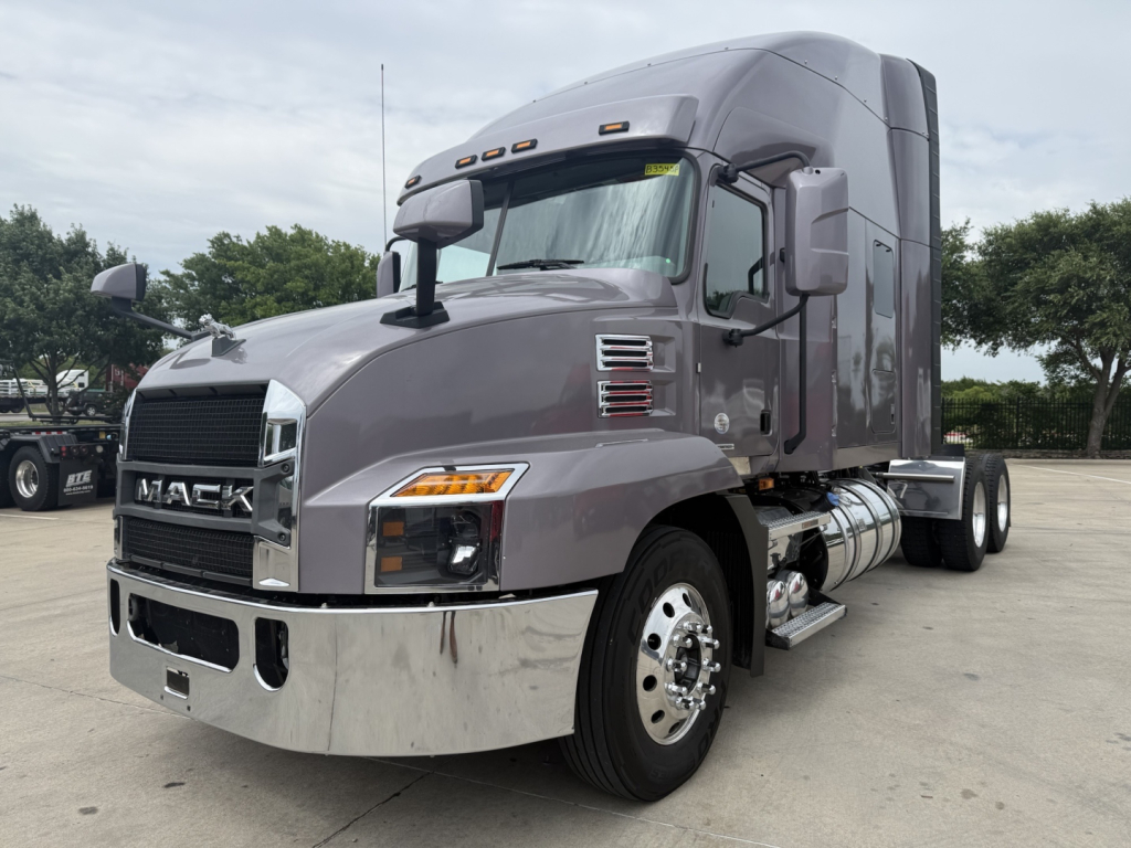 Mack AN64T70 conventional sleeper truck in showroom with gray exterior and chrome bumper showing front grille and side fuel tanks.