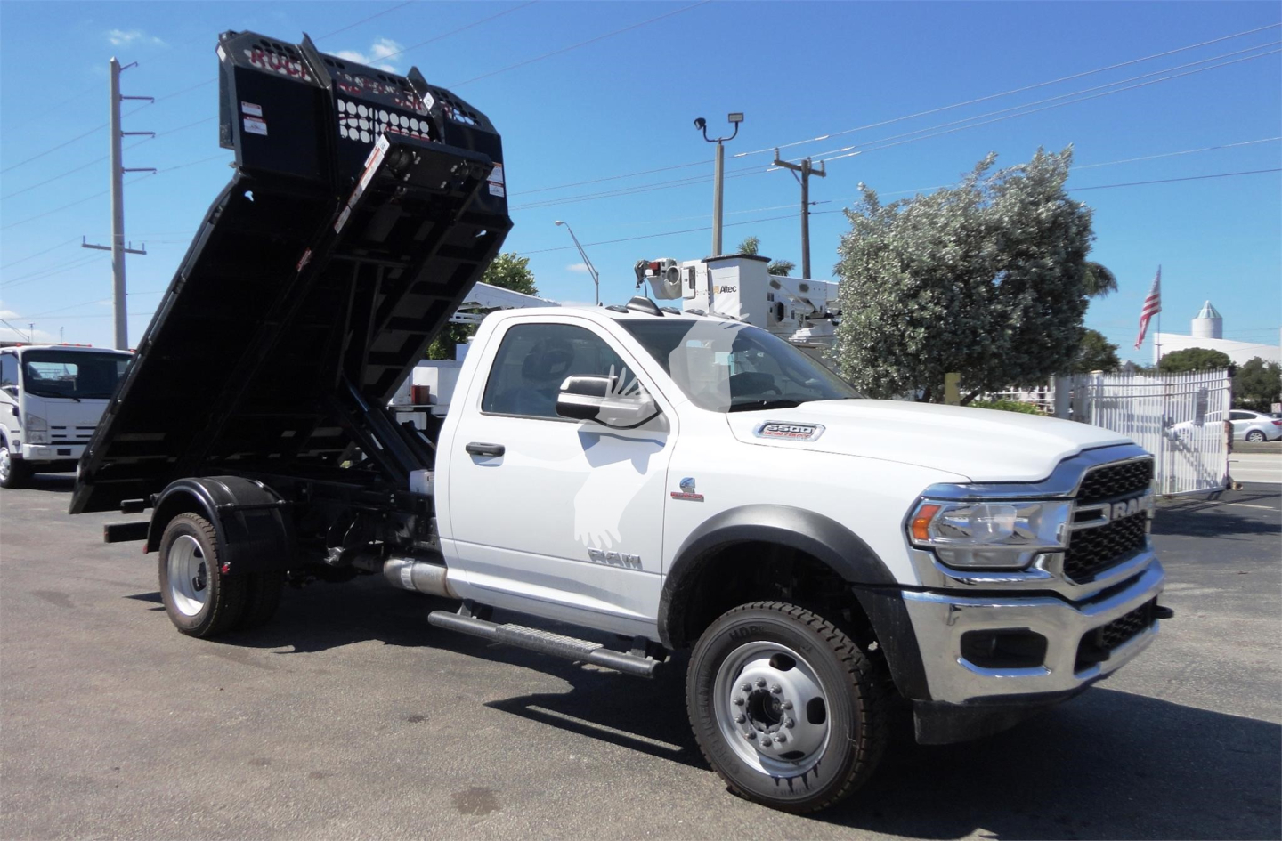 Ram 5500 dump truck with raised hydraulic bed in-service showing front and side view and stock area.